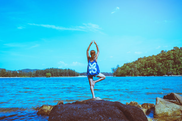亚洲女人在假期旅行放松。练习瑜伽。在海边的岩石上。图片下载