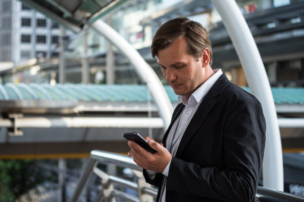 美国职业商人使用智能手机。中年经理在办公楼外拿着智能手机用应用程序发短信。图片下载