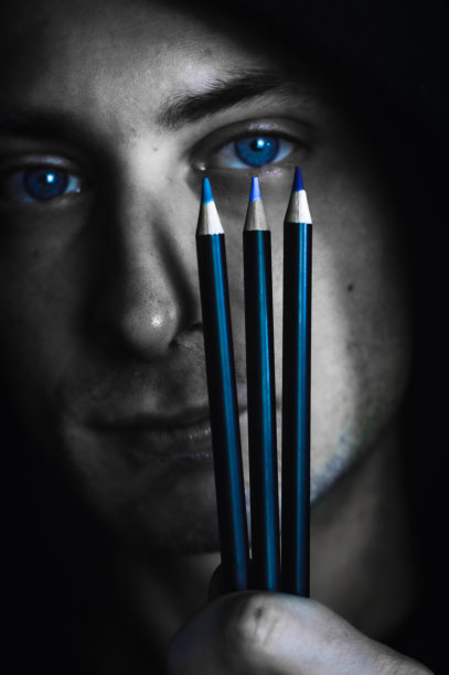 匹配的颜色-黑色和白色的肖像，一个年轻的蓝眼睛的男人拿着三支彩色铅笔在他的眼睛附近找到正确的阴影图片下载