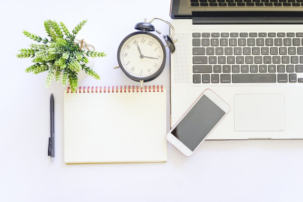 白色的桌子上放着笔记本、钢笔、智能手机和绿色植物。图片下载