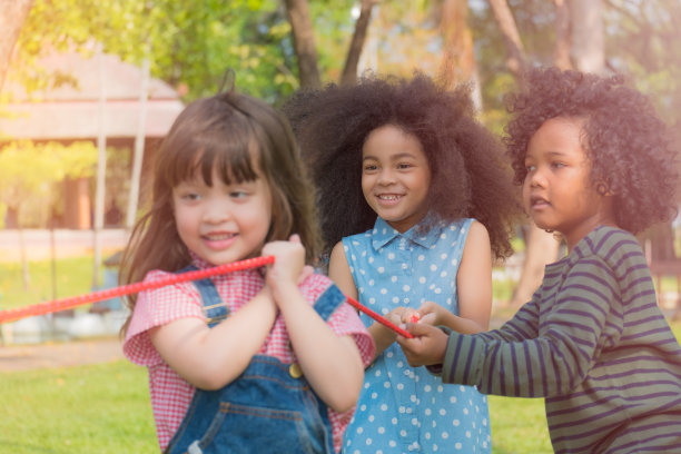 男孩和女孩在公园里拉着长长的红绳子，玩拔河游戏，看起来他们很开心，很高兴和朋友一起玩图片下载