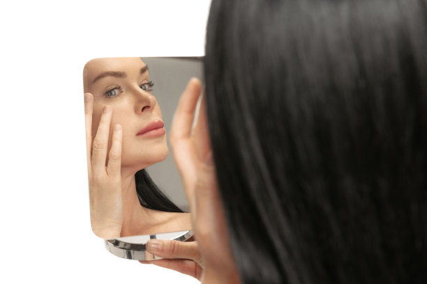 中年特写肖像，44岁的美丽的女人，黑色的长发看着她的脸在镜子里。美容，年龄相关的变化，整容和皮肤护理的概念。图片下载
