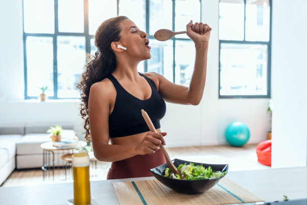 美丽的年轻女子一边做饭一边唱歌，在家里的厨房里戴着耳机听音乐。图片下载
