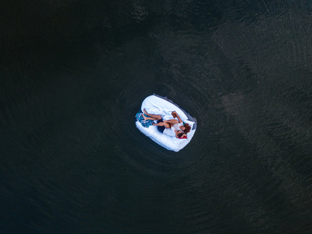 年轻夫妇躺在床垫上，白色的被褥漂浮在水面上。无人机视角图片下载