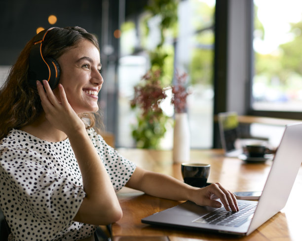 戴着无线耳机在咖啡馆或办公室用笔记本电脑工作的女商人图片下载