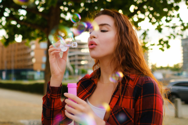 红头发的女孩，穿着红色朴素的衬衫，站在街上吹着泡泡图片下载