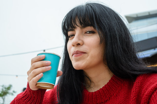 年轻的拉丁女子一边喝着热咖啡，一边淘气地看着镜头图片下载