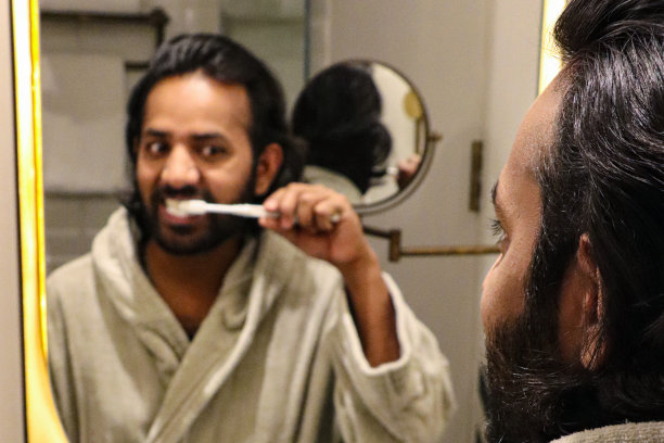 全画幅印度男子站在浴室里，穿着浴袍刷牙，牙膏和手动牙刷，漱口，剃须镜，牙齿护理，自我护理和美容的概念图片下载