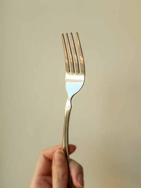 年轻女性手指上的银色叉子特写，米色调。图片下载