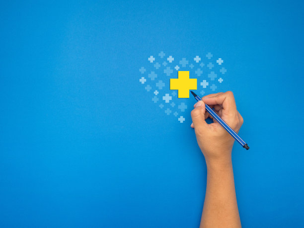 手里拿着一支笔，在蓝色的背景上画着一个黄白相间的十字图片下载