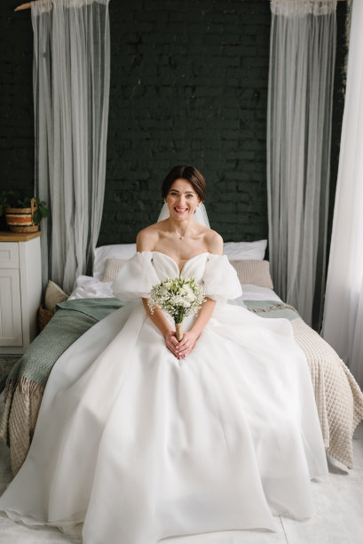 新娘穿着时髦的礼服坐在家里的床上。年轻的时尚模特，完美的皮肤和专业的化妆。奢华的婚礼。时尚照片。等待新郎。时尚的婚礼风格照片。图片下载