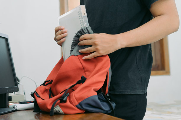 一个年轻人把一本书装进房间里桌子上的一个袋子里图片下载