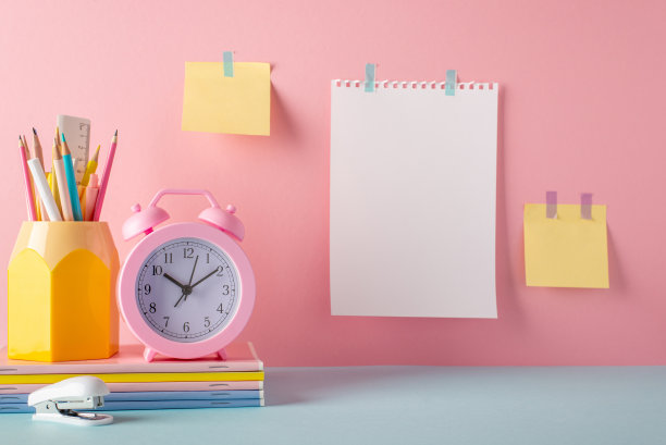 学校用品概念。笔筒、闹钟、笔记本、订书机、便签和纸的照片，贴在粉红色的墙上，留白图片下载