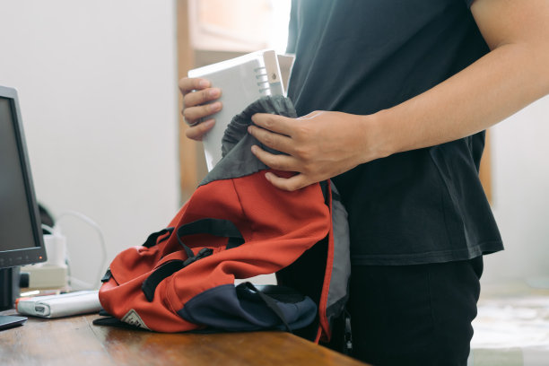 一个年轻人把一本书装进房间里桌子上的一个袋子里图片下载