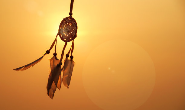 夕阳下的捕梦网，用白色的羽毛线和串珠线。手工制作的追梦人。夕阳的余晖。图片下载