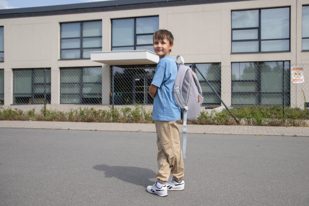 理念教育，返校，学年。有一个穿着蓝色t恤和浅色裤子的8岁男孩站在学校附近。温暖的一天。图片下载