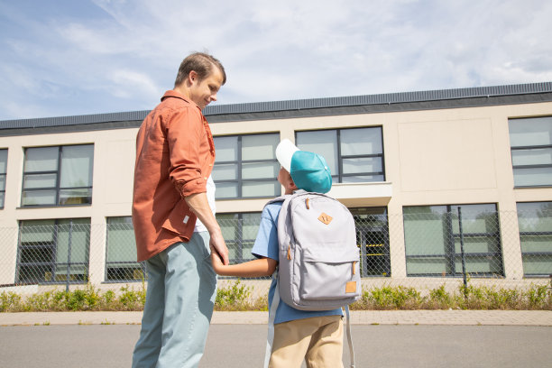 父亲送男孩去学校。爸爸握着儿子的手。父母关爱，返校，教育。温暖的晴天图片下载