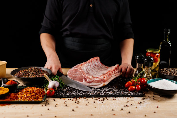 生排骨加香料，盐和迷迭香在深色木制背景。概念与男性厨师的手。图片下载