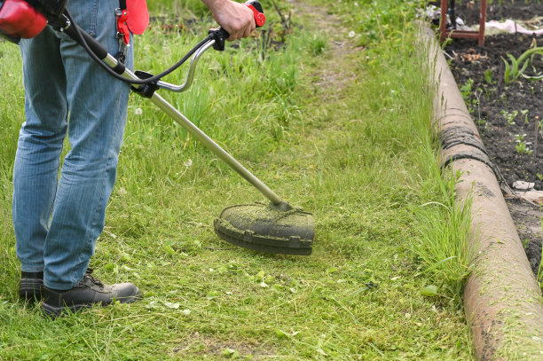 一个男人在花园里用一把汽油大镰刀割草图片下载