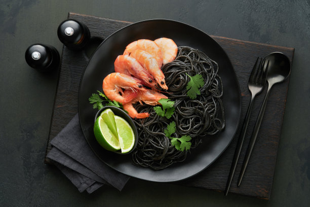 黑色的意大利面，意大利面虾在黑色的盘子上，黑色的混凝土桌子背景。鱿鱼墨对虾意面。意大利海鲜。黑色石桌的俯视图。地中海传统菜肴。图片下载