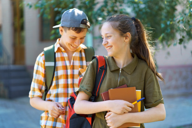 学生，一个十几岁的男孩和一个女孩走在街上，玩得开心，聊天，看书，一个明媚的夏日在城市公园图片下载
