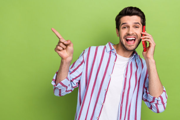 照片中，穿着条纹衬衫的男子对着智能手机说话，在绿色背景的大甩卖空地上说话图片下载