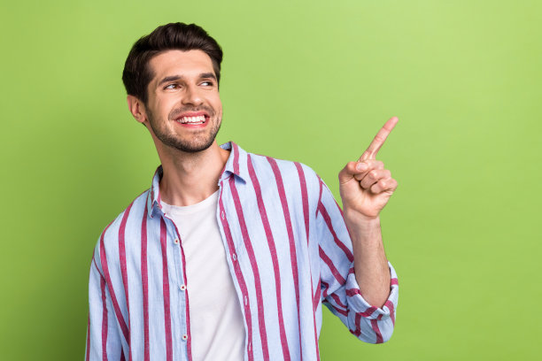 照片中的英俊男子，时尚的发型，穿着条纹衬衫，看起来在绿色的背景上指导空白的空间宣传图片下载