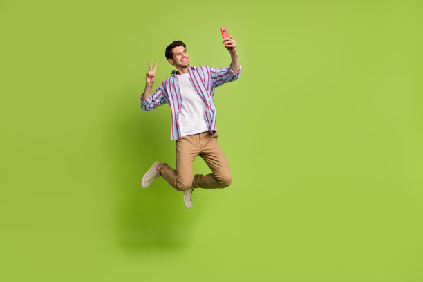 时髦年轻人的全身照片，正跳着，露出v字，博主在绿色背景下录制视频自拍图片下载