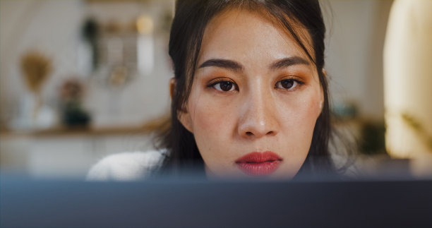 年轻的亚洲女士自由职业，专注于在笔记本电脑上的会计和财务项目的演示工作，在家里的厨房与公司进行远程会议。图片下载