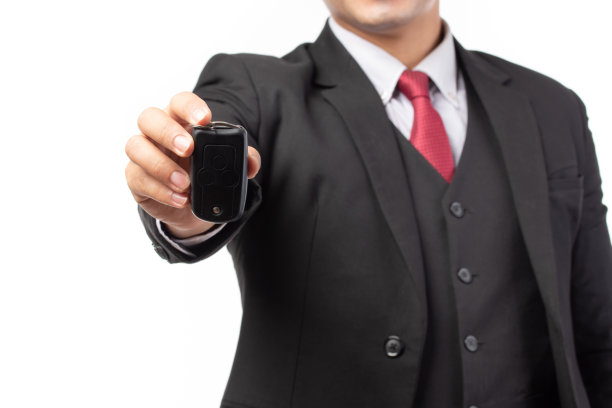 一个自信的商人的肖像在黑色西装拿着汽车的钥匙孤立在白色背景。图片下载