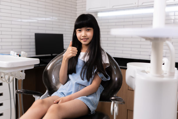 儿童牙科，牙齿健康。特写快乐的亚洲小女孩微笑着看着镜头，坐在牙医的椅子上，接受牙科治疗。图片下载