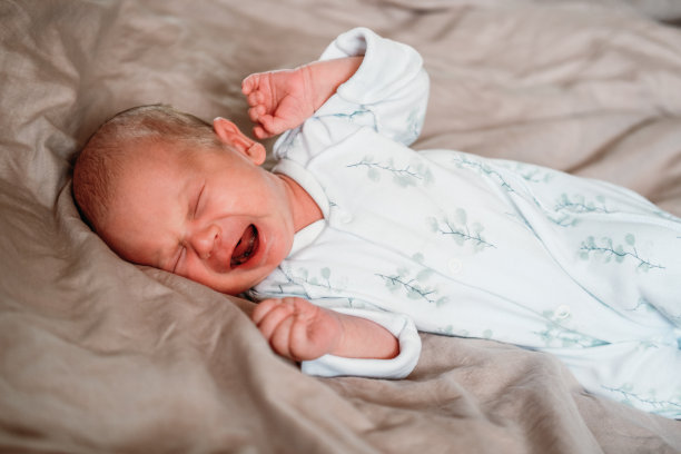 刚出生的小男孩躺在白色的床上哭泣图片下载