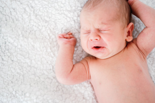 刚出生的小男孩躺在白色的床上哭泣图片下载