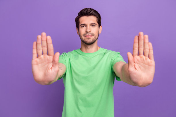 照片中，一个严肃自信、留着胡茬的男人穿着绿色t恤，在紫色的背景下伸出双臂阻止你图片下载