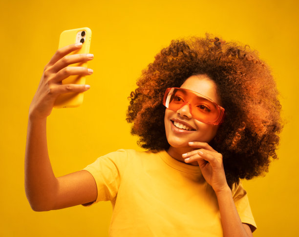 年轻的黑皮肤快乐的黑白混血女人，留着非洲发型，在脸前拿着现代手机图片下载