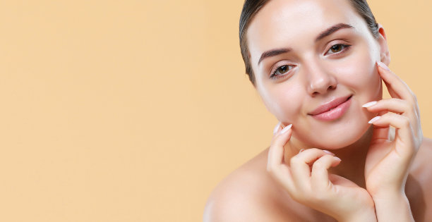 美丽的年轻女子干净新鲜的皮肤触摸她的脸在米色背景。图片下载