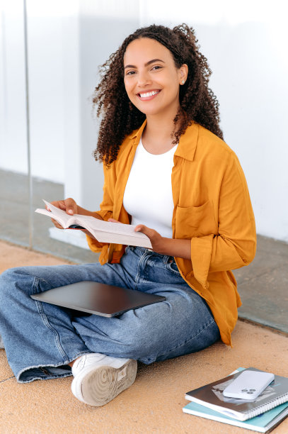 一个可爱时髦的卷发巴西或西班牙女学生的垂直照片，坐在大学校园附近，看书，准备考试，做作业，看着和微笑的镜头图片下载