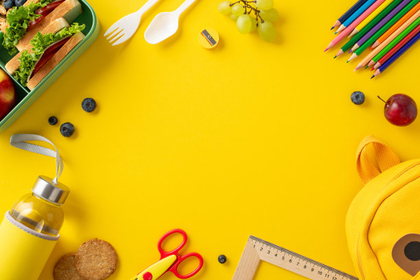 为学校准备的健康膳食。可持续午餐盒的俯视图，包括天然零食，饼干，水瓶，餐具，艺术工具，充满活力的黄色背景上的时尚背包，文字空间图片下载