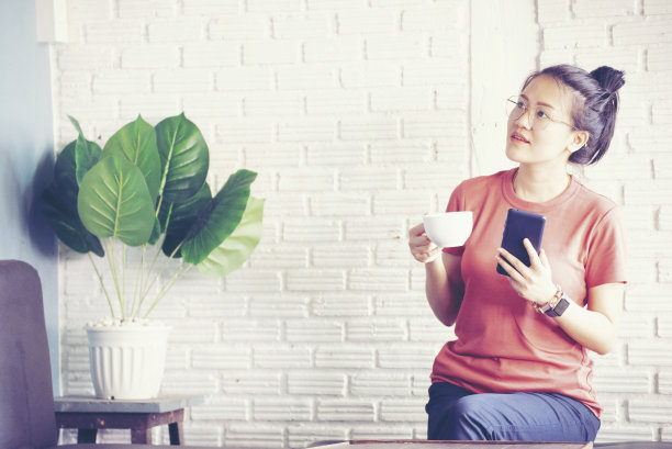 快乐的年轻女性工作方式自由职业者放松和chill喝咖啡在客厅，自然花园的背景。生活方式的概念图片下载