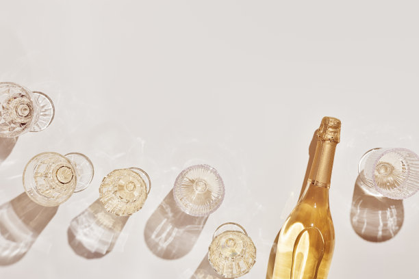 夏日聚会酒水平铺，酒杯里装着白色的气泡酒和阳光的影子放在浅色的桌子上。最小的图案与美丽的酒杯，上面看静物，米黄色的金色图片下载