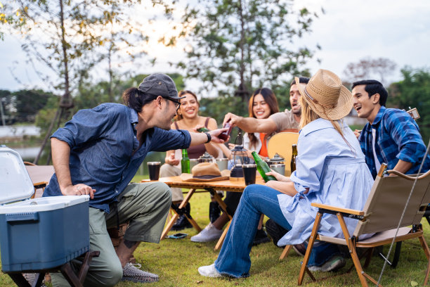 一群不同的朋友一起在帐篷里举行户外露营聚会。有魅力的年轻男女旅行者喝着酒精啤酒，享受在森林度假旅行中闲逛。图片下载
