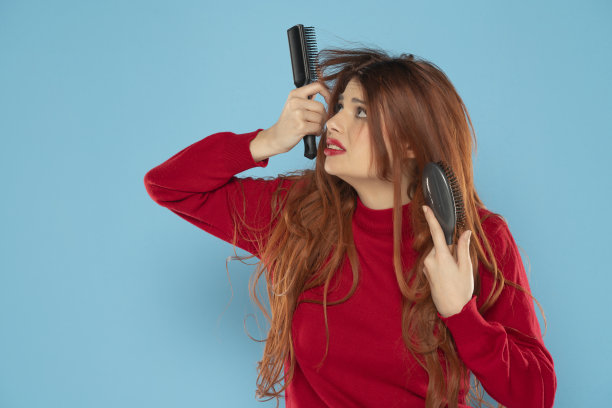 一个紧张的年轻红发女人，在蓝色背景下凌乱的头发上插着刷子图片下载