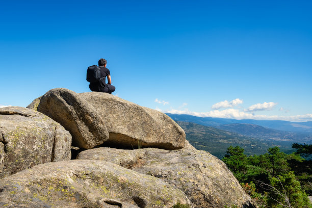 马德里瓜达拉马，一名男子坐在一些大岩石上，凝视着美丽的山景。图片下载