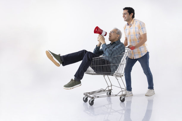 坐在购物车里拿着扩音器的老人和推着购物车的年轻人被隔离在白色背景中。图片下载
