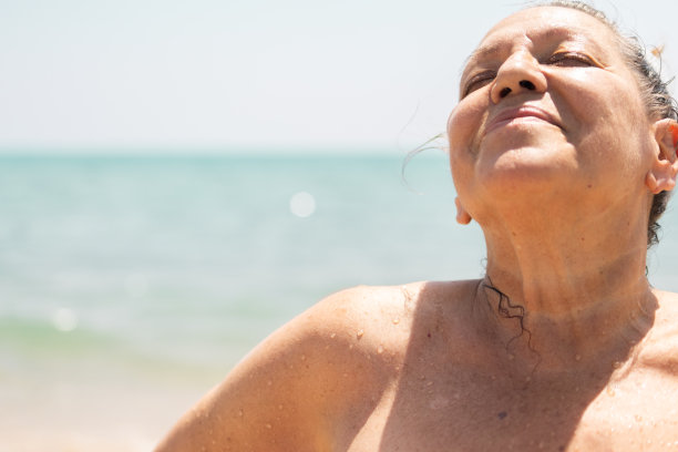 一位年长的成年妇女在海滩上微笑着，她游泳后的皮肤被海水滴湿了。夏季概念和日光浴。图片下载
