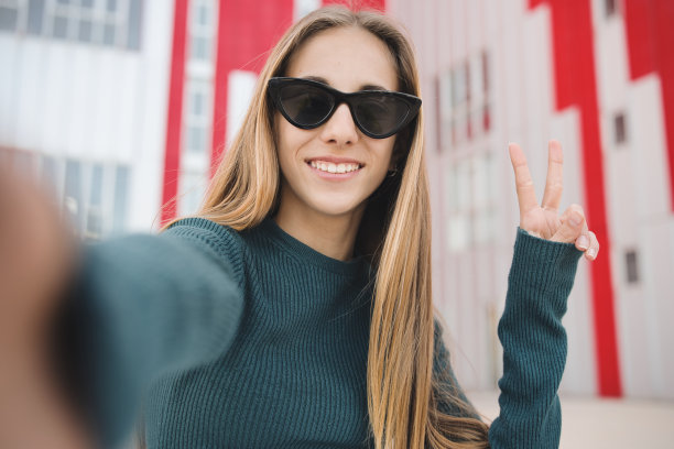 戴着墨镜的金发少女在校园里开心地自拍。一个兴奋的白种人看着摄像机拍下的户外和平标志。图片下载