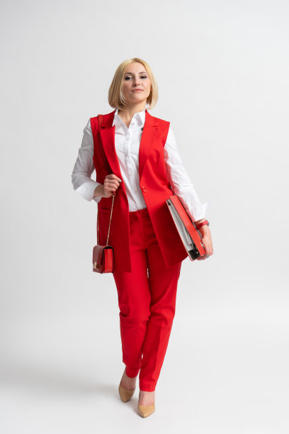 年轻的商务女性穿着红色休闲长裤套装，带着办公文件夹和手提包图片下载
