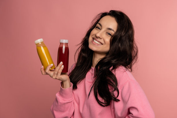 快乐的黑发年轻女子一手拿着几瓶软饮料在摄影棚拍摄。健康饮品概念图片下载