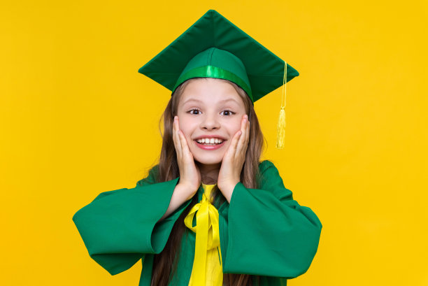 穿着毕业服装的孩子。女学生在一年结束时欢欣鼓舞。孩子的教育。一个小女孩在孤立的黄色背景上微笑。图片下载