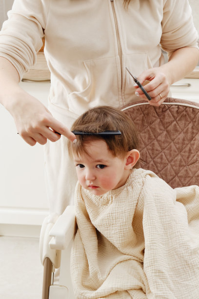 母亲在厨房里剪着蹒跚学步的男孩。自己的理发师剪小孩的头发。一岁六个月的孩子图片下载